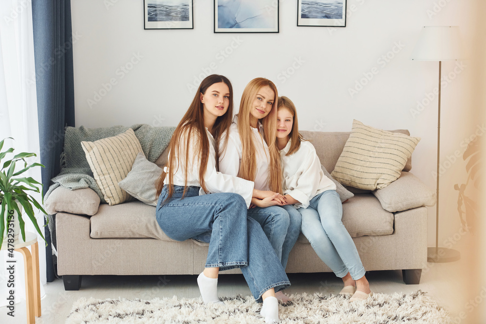Sitting on the sofa. Young mother with her two daughters at home at daytime