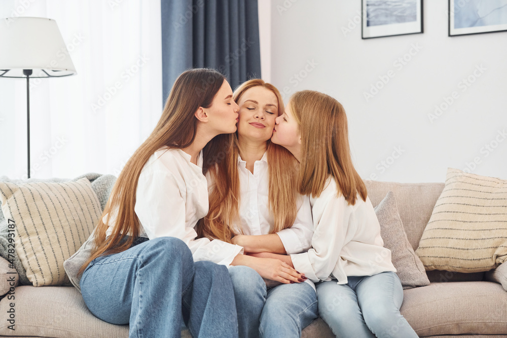 Sitting on the sofa. Young mother with her two daughters at home at daytime