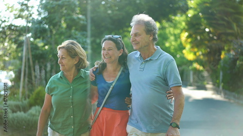 Joyful daughter walking with senior parents together in green city laughing and smiling