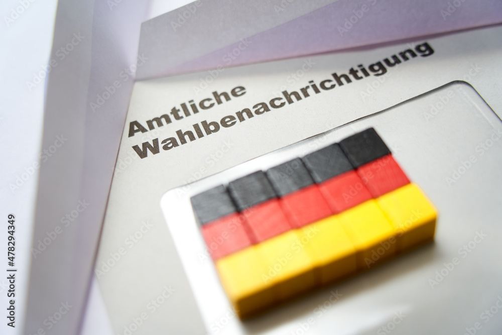 Black letters on white envelope saying: Official election notification (german: Amtliche Wahlbenachrichtigung). Wooden dice shape german national flag. 2021 federal election in germany. Closeup.