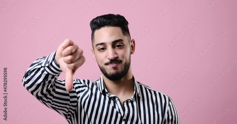 Unhappy businessman giving thumbs down gesture over pink background Unhappy businessman giving thumbs down gesture over pink background