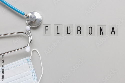 Word FLURONA on gray with face mask and stethoscope background. COVID and flu double infection. First combination of two viruses, respiratory coinfections concept. Top view, copy space photo