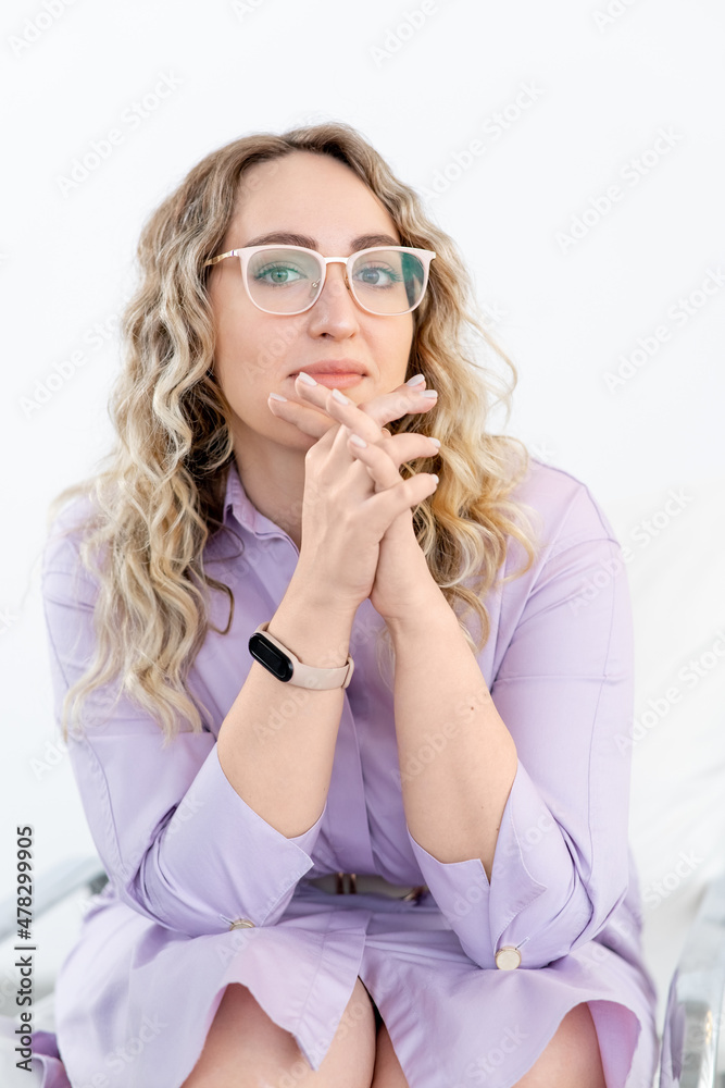 A business lady with eyeglasses looks into the camera. Light purple shirt. Consultation with a psychotherapist. White walls. There is smart watch on my hand. A business lady with eyeglasses looks into the camera. Light purple shirt. Consultation with a psychotherapist. White walls. There is smart watch on my hand.