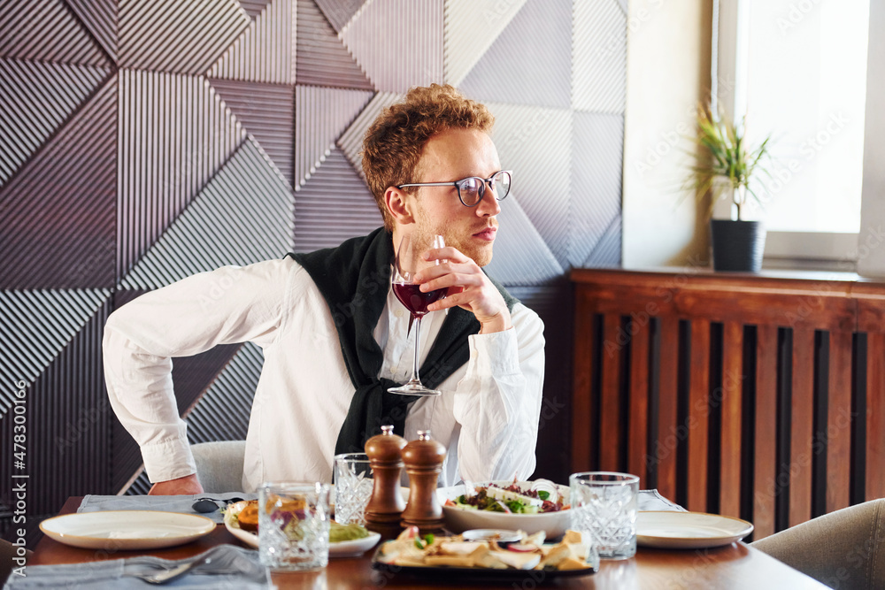 Man in glasses sits by the table. Indoors of new modern luxury restaurant Man in glasses sits by the table. Indoors of new modern luxury restaurant