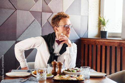 Man in glasses sits by the table. Indoors of new modern luxury restaurant