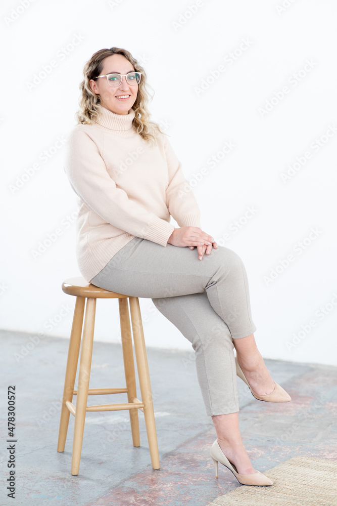Happy obese woman with glasses in warm sweater sits on stool