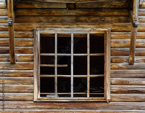Window frame with broken glass in the wall of an old abandoned wooden house. The picture was taken in the village of Pervokrasnoe, in the Orenburg region