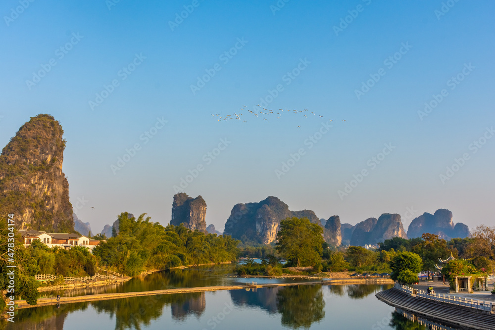Flock of birds flying over the Li River in Yangshuo at sunset, China