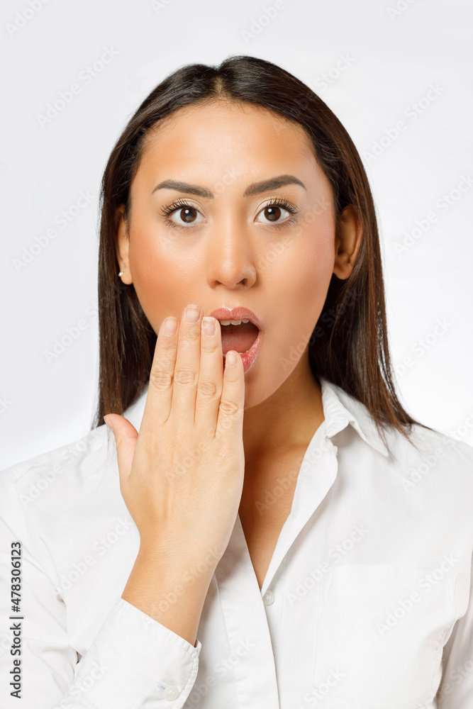 Surprised young woman with wide open eyes covering mouth with her hand and looking at camera while standing isolated against white background Surprised young woman with wide open eyes covering mouth with her hand and looking at camera while standing isolated against white background