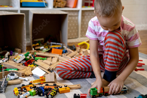 Kids play with wooden railway. Child with toy train. Cute kid playing cars and engine. Educational toys young children.