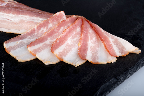Slices of fresh juicy bacon on a black cutting board