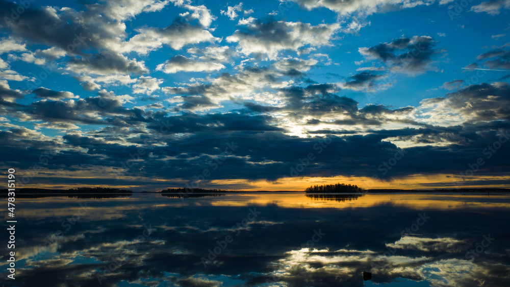 Morning light reflection in lake Malaren in Sweden, Sky reflected in calm water dramatic clouds, Golden horizon with dark silhouette of islands, Scandinavia winter gorgeous sunrise