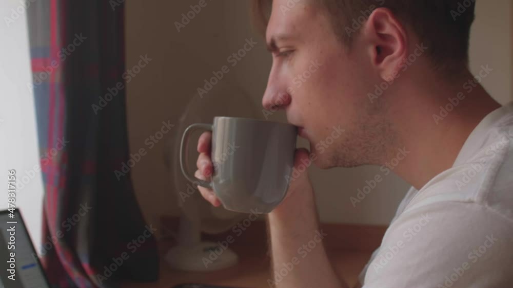 The man takes a mug of drink with his hands. Against the background of a laptop. He is drinking a hot drink. Free time during the break. The man takes a mug of drink with his hands. Against the background of a laptop. He is drinking a hot drink. Free time during the break.