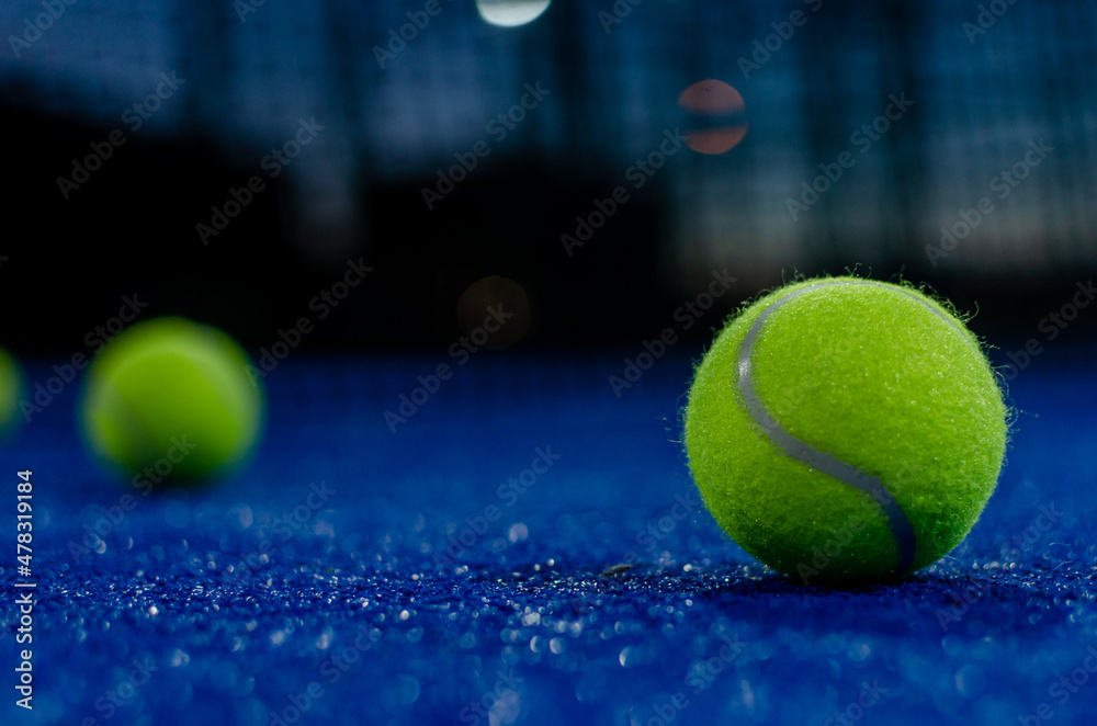 Selective focus. Two paddle tennis balls on a blue paddle tennis court at night.