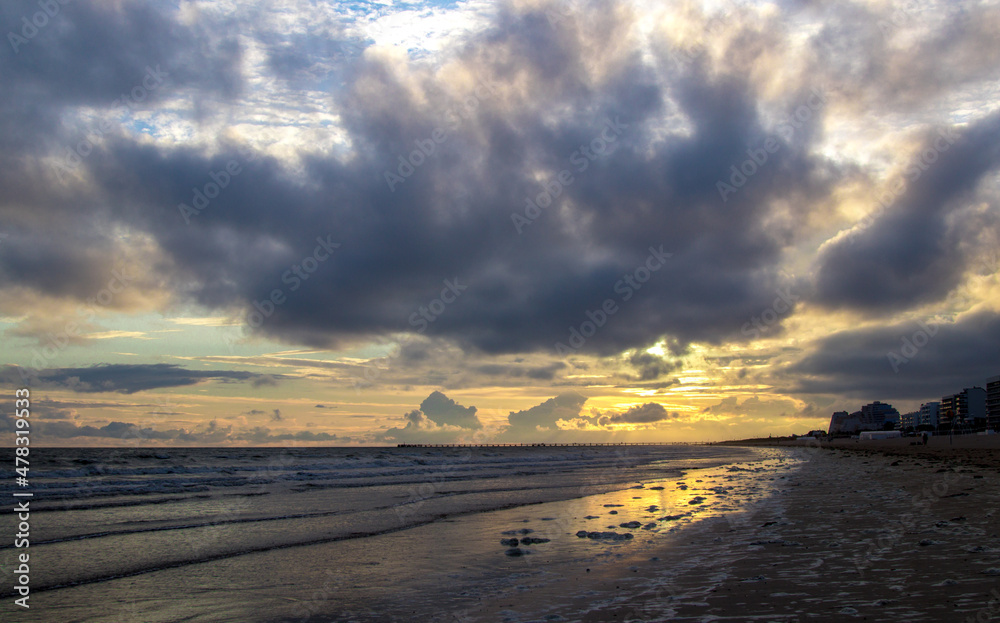 Sunset over a French beach with impressive cumulus clouds filtering the light.