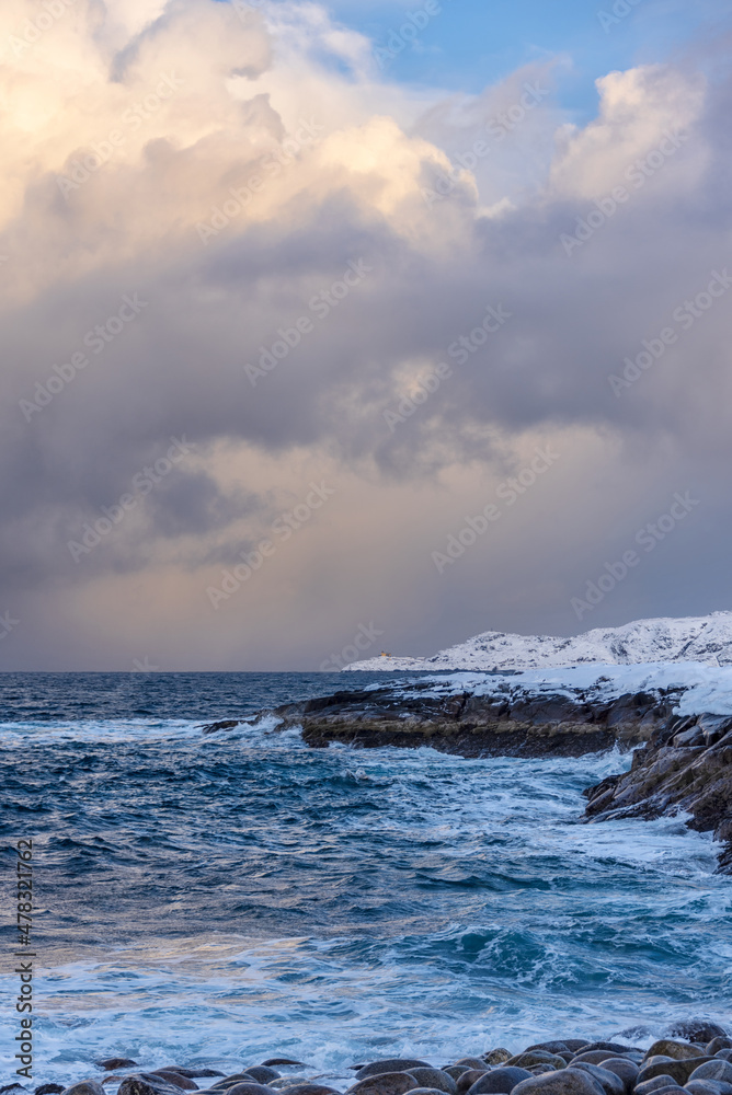 Winter Sea with snow covered rocky shores and a small lighthouse on a promontory in the distance