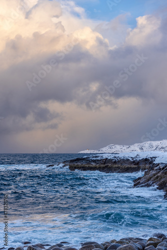Winter Sea with snow covered rocky shores and a small lighthouse on a promontory in the distance