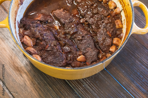 A yellow dutch oven with homemade braised beef short ribs in wine and garlic
