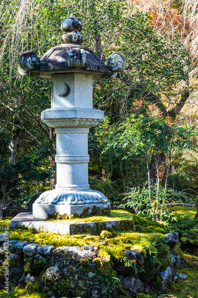 A Japanese garden shrine in a forest and covered with moss with sunlight shining through at the Tenryu-Ji Temple.