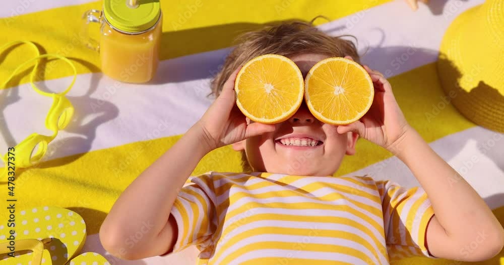Happy child holding halves of orange fruit like a sunglasses. Slow motion