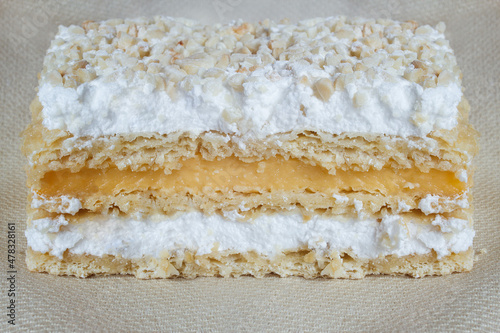 Close-up detail of crunchy overlapping layers of puff pastry millefeuille, filled with cream and meringue, and covered with chopped and au gratin almonds on a texture background. Traditional desserts.