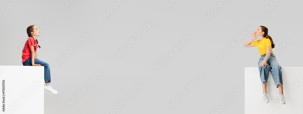 Two little girls sit opposite each other and communicate isolated on gray studio background. Emotions, facial expression, childhood concept Two little girls sit opposite each other and communicate isolated on gray studio background. Emotions, facial expression, childhood concept
