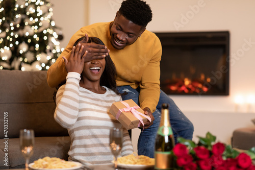 African Husband Surprising Wife With Gift Covering Her Eyes Indoor