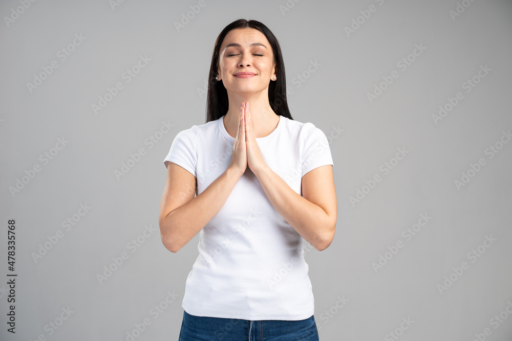 Young brunette woman practicing yoga, holding hands in namaste and keeping her eyes closed. Caucasian girl meditating indoors, praying for peace and love, having calm and peaceful facial expression Young brunette woman practicing yoga, holding hands in namaste and keeping her eyes closed. Caucasian girl meditating indoors, praying for peace and love, having calm and peaceful facial expression