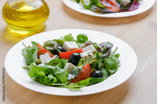 Fresh Greek salad in white plate at wooden table background. Closeup top view.