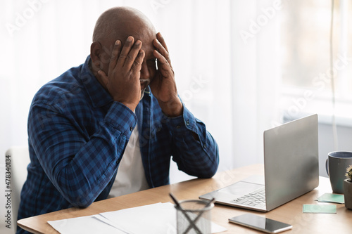 Unhappy Senior Black Businessman Covering Face Sitting Near Laptop Indoor