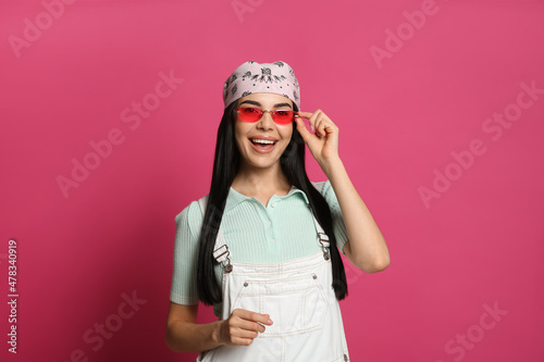 Young woman wearing stylish bandana and sunglasses on pink background