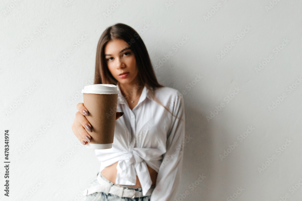 Young pretty woman offering a brown cup of coffee looking to the camera over white background. Young caucasian woman serving fresh hot coffee Young pretty woman offering a brown cup of coffee looking to the camera over white background. Young caucasian woman serving fresh hot coffee