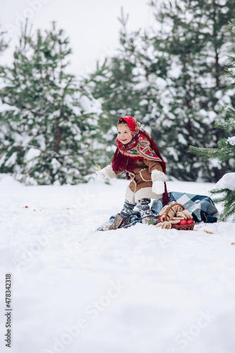 Beautiful little child girl plays in snowy forest in red headscarf.