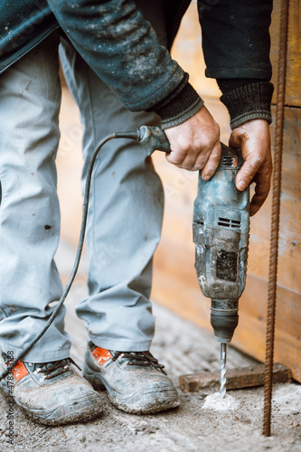 Builder working with rotary hammer drill perforator equipment making holes in concrete on construction site photo