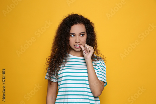 African-American woman biting her nails on yellow background