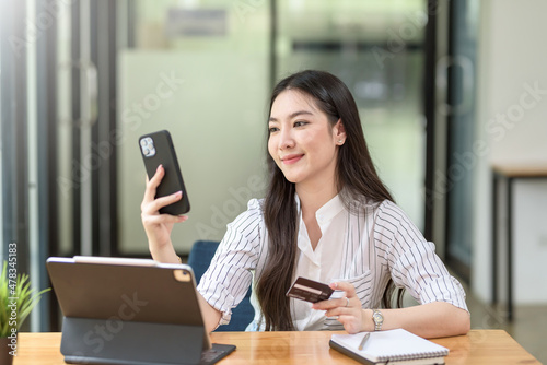 Beautiful young Asian woman holding smartphone and using credit card for online shopping.