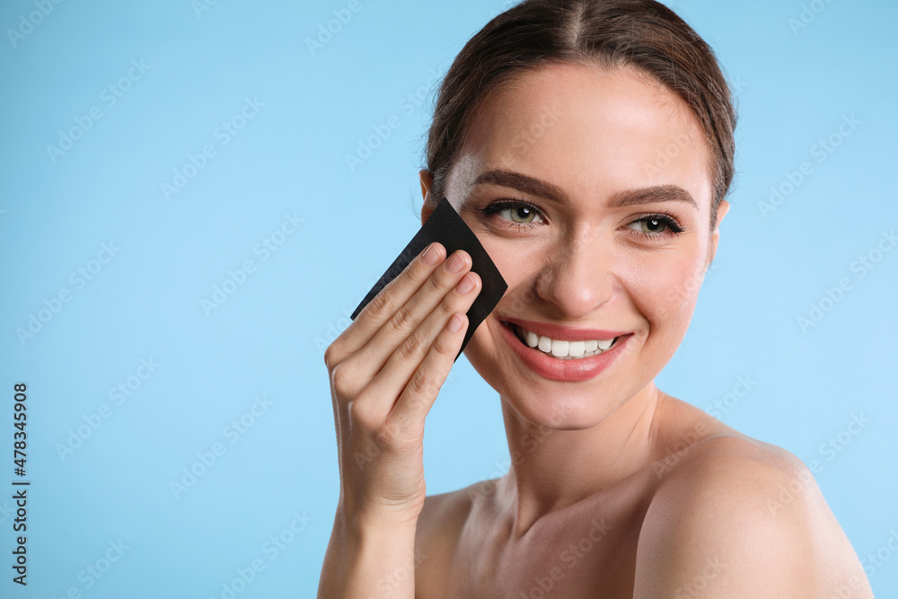 Beautiful woman using mattifying wipe on light blue background, space for text Beautiful woman using mattifying wipe on light blue background, space for text