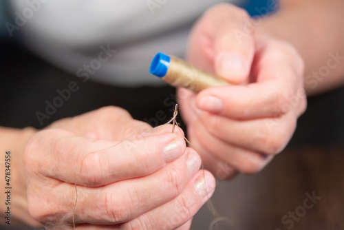 An elderly lady is holding a thread and a needle. Sews.