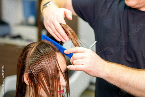 The hairdresser cuts the hair of a brunette woman. Hairstylist is cutting the hair of female client in a professional hair salon, close up