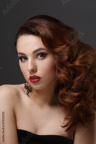 Fashion beauty portrait of a beautiful girl with curly hair luxuriant on a dark background.