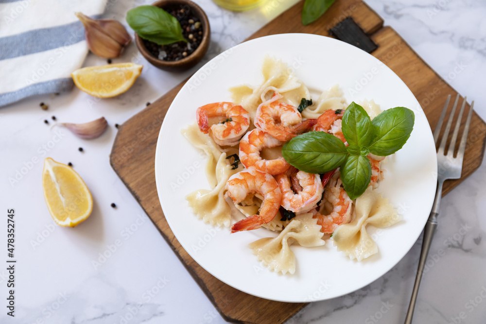 Mediterranean cuisine, seafood diet. Italian farfalle pasta with prawns garlic, basil and lemon on a marble tabletop.