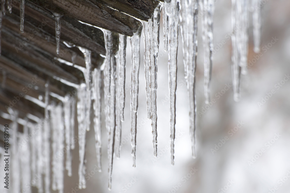 Thaw and ice melting. The icicles are melting from eaves of roof in spring. Drops of water fall of a roof. The end of winter. Blurred background. Thaw and ice melting. The icicles are melting from eaves of roof in spring. Drops of water fall of a roof. The end of winter. Blurred background.