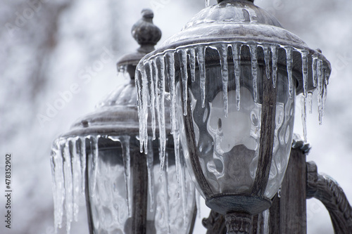 Ice-covered street light with icicles, close up. Icing  city park on a winter day after freezing rain in Mykolaiv. Blurred background. photo