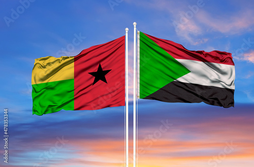 Sudan and Guinea Bissau two flags on flagpoles and blue cloudy sky