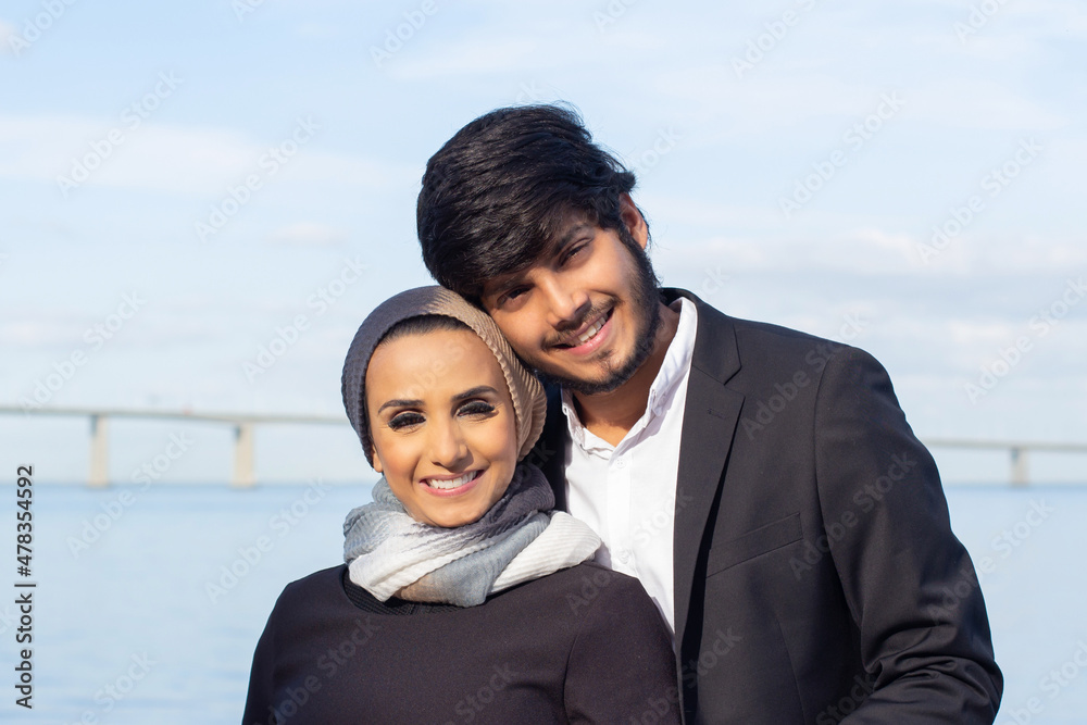 Portrait of loving Arabic couple during walk. Woman with covered head and bright make-up and man in suit smiling at camera, hugging. Love, affection concept Portrait of loving Arabic couple during walk. Woman with covered head and bright make-up and man in suit smiling at camera, hugging. Love, affection concept
