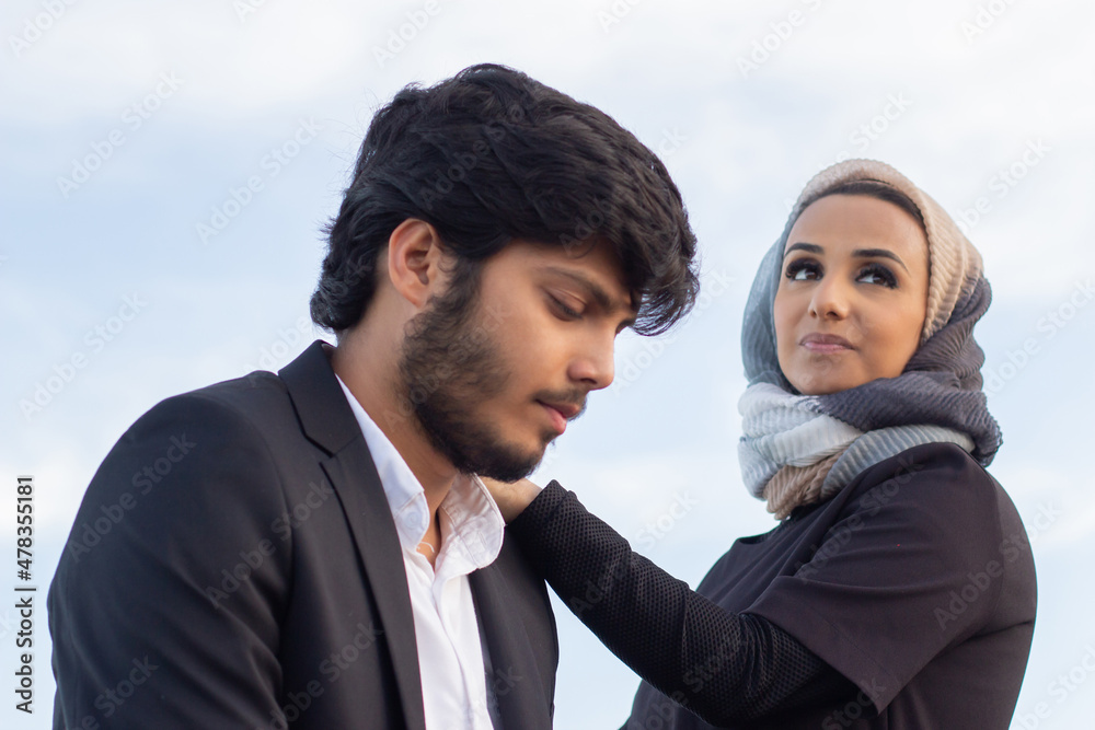 Loving Arabic couple spending time together. Woman with covered head and bright make-up and man in suit walking on bridge. Love, affection concept Loving Arabic couple spending time together. Woman with covered head and bright make-up and man in suit walking on bridge. Love, affection concept