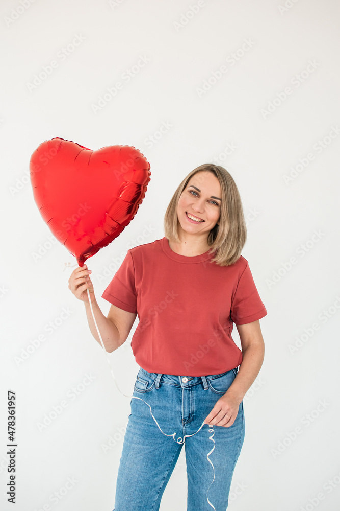 A woman in blue jeans and a red t-shirt is smiling and holding a red heart-shaped balloon. Happy Valentine's Day A woman in blue jeans and a red t-shirt is smiling and holding a red heart-shaped balloon. Happy Valentine's Day