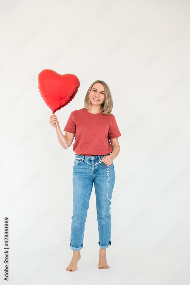 Full-length portrait of a woman in blue jeans and a red T-shirt with a heart-shaped balloon on a white background. Happy Valentine's Day Full-length portrait of a woman in blue jeans and a red T-shirt with a heart-shaped balloon on a white background. Happy Valentine's Day