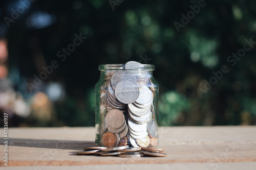 Plant growing in saving coin in glass jar placed on wooden floor and green blur background, save and make a profit with interest,Growing Money,money saving,finance and investment idea.