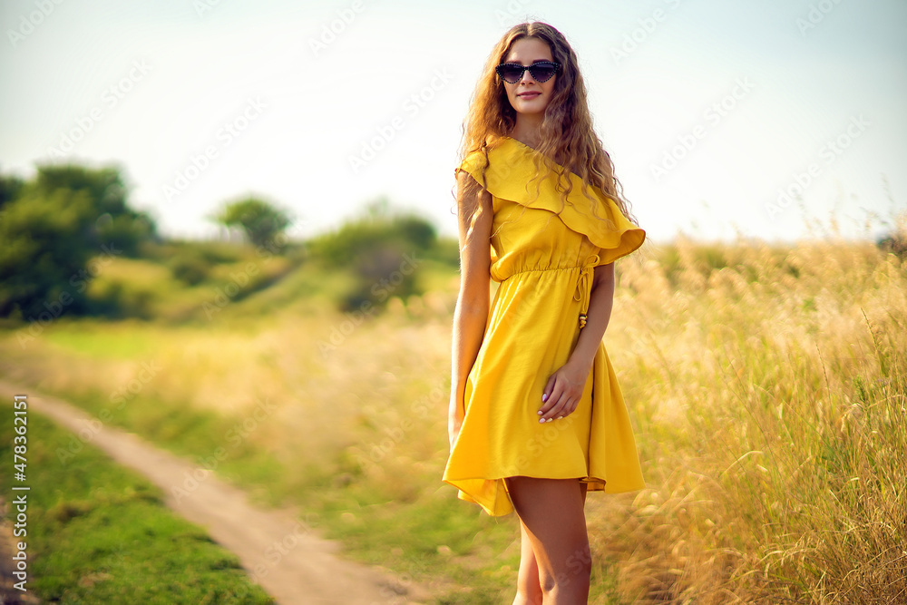 Beautiful curly girl walks on field in summer while wearing a sunglasses and yellow dress. Lifestyle Beautiful curly girl walks on field in summer while wearing a sunglasses and yellow dress. Lifestyle